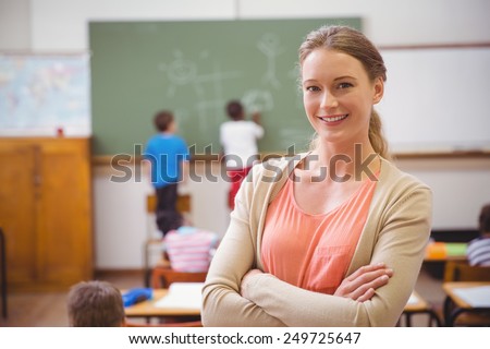 Pretty teacher smiling at camera at back of classroom at the elementary school