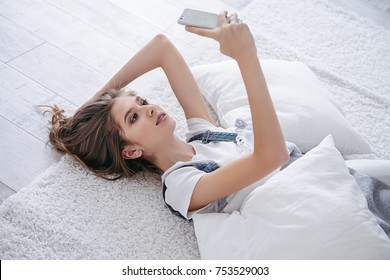 Pretty teen girl makes selfie on her smartphone while laying in a bedroom. Healthcare, stomatology and orthodontics.