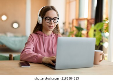 Pretty Teen Girl In Wireless Headset Using Laptop, Interested Happy Student Typing On Keyboard Looking At Pc Screen, Having Online Course Or Doing Homework