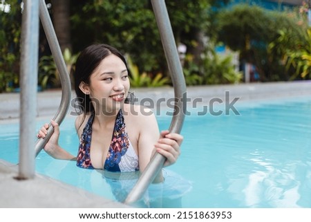 A pretty teenage asian lady in a bikini top and shorts climbing a pool ladder after a swim. Vacationer at a resort or hotel.