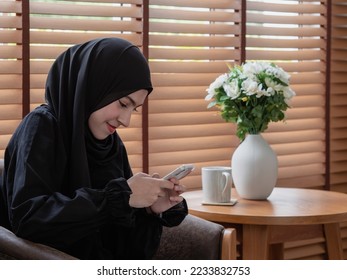 Pretty teenager girl using mobile phone while sitting at coffee table at home. - Shutterstock ID 2233832753