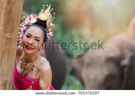 Pretty thai girls in traditional thai costumes touch a tree with elephants background
