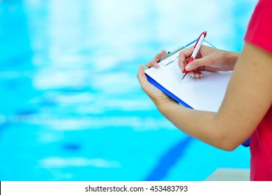 Pretty trainer looking at stopwatch at the pool - Powered by Shutterstock