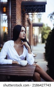 Pretty trendy girl drinking coffee in street cafe. Portrait of brunette young model woman.  - Shutterstock ID 2186427743