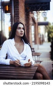 Pretty trendy girl drinking coffee in street cafe. Portrait of brunette young model woman.  - Shutterstock ID 2195098143