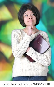 A Pretty Tween Girl Thinking While Holding Her Bible Before A Large, Stained Glass Window.