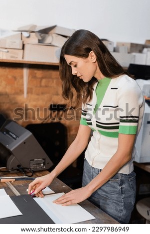 pretty typographer holding knife near paper while working in print center
