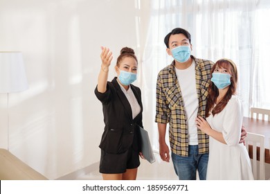 Pretty Vietnamese Female Real Estate Agent Showing New House To Young Couple In Medical Mask