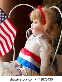 A Pretty Vintage Doll Is Dressed For The Fourth Of July, Gazing Out A Window With An American Flag.