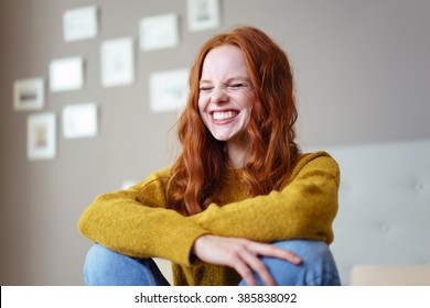 Pretty vivacious young woman laughing with her eyes screwed closed in a candid moment of fun and hilarity as she sits on her bed at home - Shutterstock ID 385838092