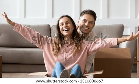 Pretty wife sit inside of carton box raised outstretched arms like flying plane wings dreaming with husband happy life at new own first house, planning vacation daydreaming about future travel concept