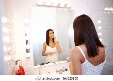 Pretty woman applying makeup in bathroom mirror.