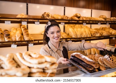 Pretty woman in apron selling freshly baked pastry and bread in bakery shop. - Powered by Shutterstock