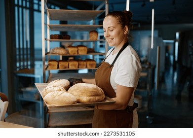 Pretty woman baker holding variety of baked bread on tray - Powered by Shutterstock