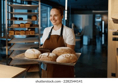 Pretty woman baker holding variety of baked bread on tray - Powered by Shutterstock