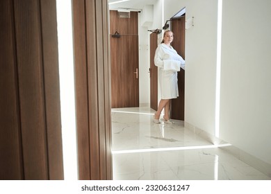 Pretty woman in a bathrobe stands in a bright corridor - Powered by Shutterstock