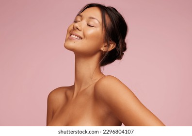Pretty woman with beautiful and glowing skin. Female model with eyes closed and smiling against pink background.