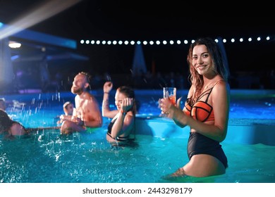 Pretty woman in bikini drinking cocktail and hanging out with friends at night pool party. People having fun dancing with drinks and splashing water in luxury private villa swimming pool. - Powered by Shutterstock