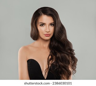Pretty woman brunette with long healthy shiny dark brown wavy hair, clean skin and makeup on gray background. Beauty fashion portrait, haircare concept