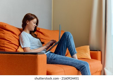 Pretty Woman Chatting On The Orange Couch With A Laptop Apartments