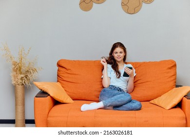 Pretty Woman Chatting On The Orange Couch With A Smartphone Apartments