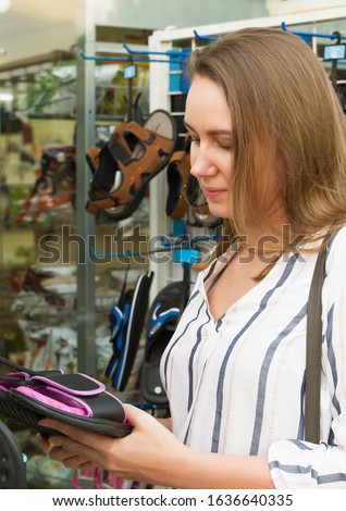 Pretty woman choosing flip-flops in shop on vacation.