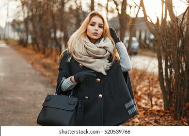 Pretty woman in a coat with a scarf and with a handbag walks in autumn park.