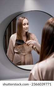 Pretty Woman Combing Her Beautiful Hair With Brush While Standing Near Mirror In Bathroom, Attractive Young Lady Looking To Her Reflection And Smiling, Selective Focus With Free Space.  - Shutterstock ID 2366039771