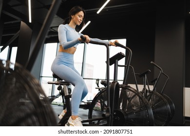 Pretty woman in crossfit gym using exercise bike for cardio workout. Sport girl on air bike - Shutterstock ID 2091807751