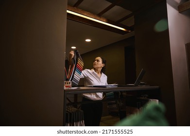 Pretty Woman Designer, Decorator Choosing Fabrics For Curtains, Pillows, Embroidery Fabrics, Carpets And Sofa Upholstery In The Textile Show Room, Standing Near A Stand With Various Fabric Swatches