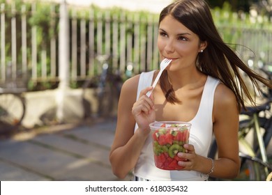 Pretty Woman Eating A Healthy Fresh Fruit Salad From A Plastic Tub Licking The Fork With Appreciation As She Stands Outdoors