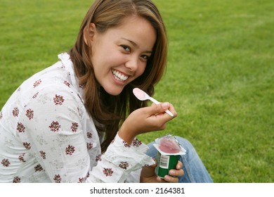 A Pretty Woman Eating Yogurt On The Grass