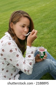 A Pretty Woman Eating Yogurt On The Grass