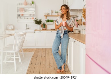 Pretty woman enjoying cozy morning on her stylish kitchen while drinking hot tea. Full length.  - Powered by Shutterstock