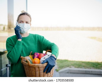 Pretty woman with face mask and green pullover and black gloves makes a phone call after shopping and is holding her shopping basket - Shutterstock ID 1703558500