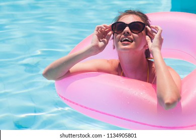 pretty woman floating with pink rubber inflatable ring in swimming pool and having fun