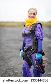 Pretty Woman Happy, Dressed In Jumpsuit And Parachute Harness On Airport Runway Ready For Skydive Jump