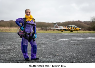 Pretty Woman Happy, Dressed In Jumpsuit And Parachute Harness On Airport Runway Ready For Skydive Jump