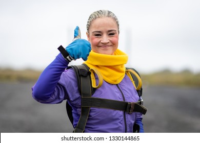 Pretty Woman Happy, Dressed In Jumpsuit And Parachute Harness On Airport Runway Ready For Skydive Jump