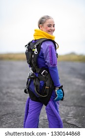 Pretty Woman Happy, Dressed In Jumpsuit And Parachute Harness On Airport Runway Ready For Skydive Jump