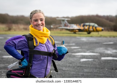 Pretty Woman Happy, Dressed In Jumpsuit And Parachute Harness On Airport Runway Ready For Skydive Jump