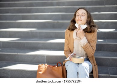 Pretty Woman Have Outdoor Lunch Near Office Building While Sitting On The Stairs. Healthy Meal For Takeaway. Removes The Protective Mask On Her Chin And Keep A Social Distance. Copy Space.