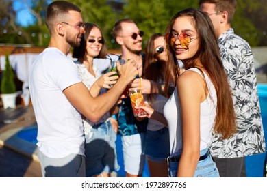 Pretty Woman Having Fun At Poolside Summer Party Clinking Glasses With Friends On Sunny Summer Day Near Swimming Pool. People Toast Drinking Fresh Juice Cocktails At Luxury Villa On Tropical Vacation.