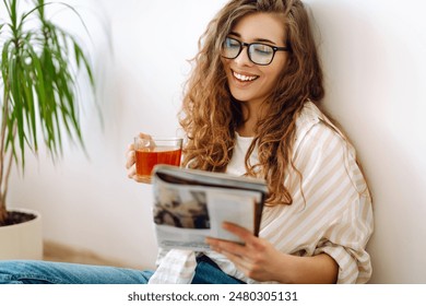 Pretty woman at home drinking tea and reading book or magazine. Domestic life. - Powered by Shutterstock