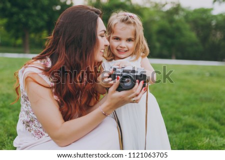 Pretty woman in light dress and little cute child baby girl take picture on retro vintage photo camera in park. Mother, little kid daughter. Mother's Day, love family, parenthood, childhood concept