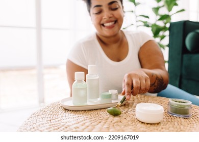 Pretty Woman In Living Room With Her Facial Massage Tools. Attractive Female Holding Using Jade Roller For Facial Skin Treatment.