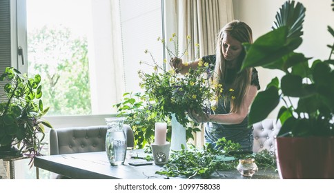 Pretty woman with long hair arranging wild flowers bunch in vase on table in living room at window with sunset light. Home lifestyle and decor ideas - Powered by Shutterstock