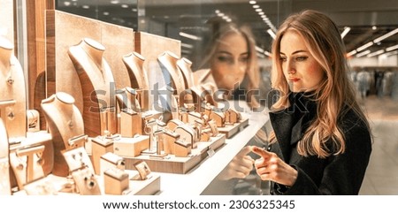Pretty woman looking at jewelry in store window. Customer near jewellery. Dreamy long haired blonde girl chooses silver, gold, diamonds, precious stones. Purchaser