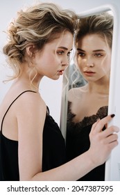 Pretty Woman Looking at Reflection in Mirror Photo. Serious Attractive Girl Examining Cosmetics on Face. Alluring and Charming Lady Model in Trendy Clothes Prepare for Romantic Dating