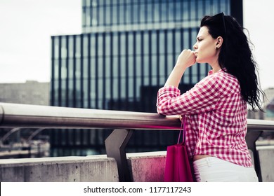 A pretty woman looks ahead with a shopping bag in her hand. The woman stands on the bridge, rests and nostalgically looks into the distance. The concept of detention, consternation. - Shutterstock ID 1177117243